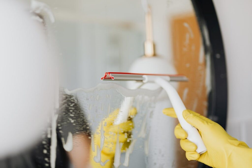 A professional cleaner wiping a mirror to remove streaks and grime